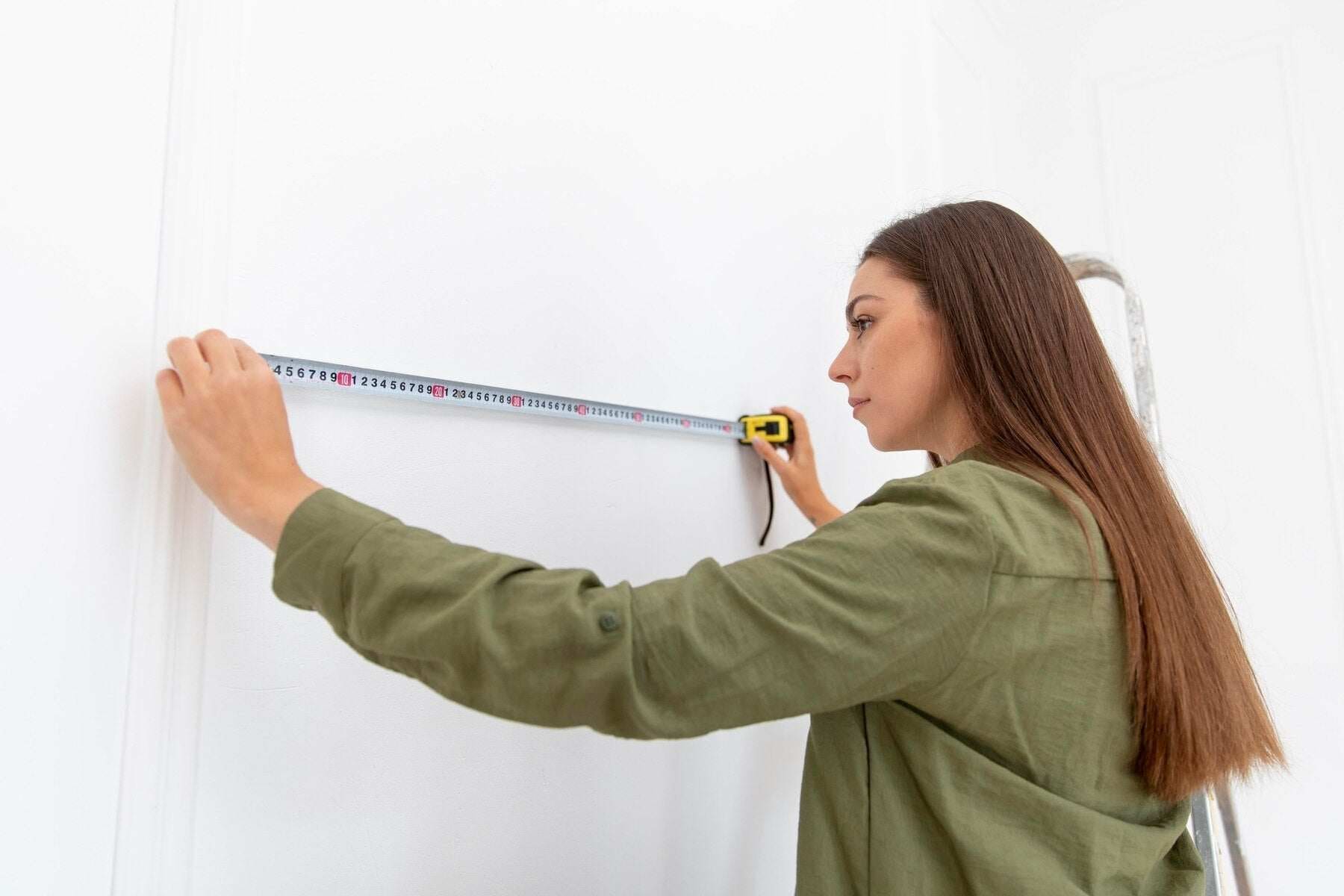 Femme mesurant un mur blanc à l’aide d’un mètre ruban rétractable