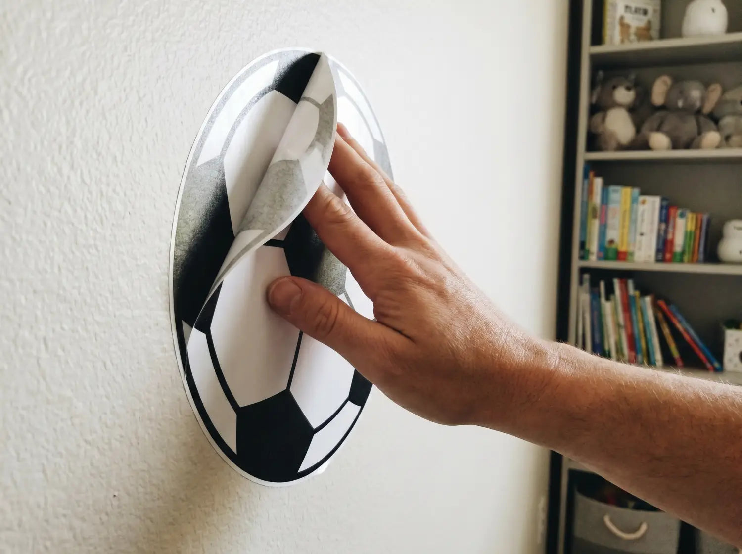 Pose d'un sticker ballon de foot sur un mur de chambre d'enfant par un parent