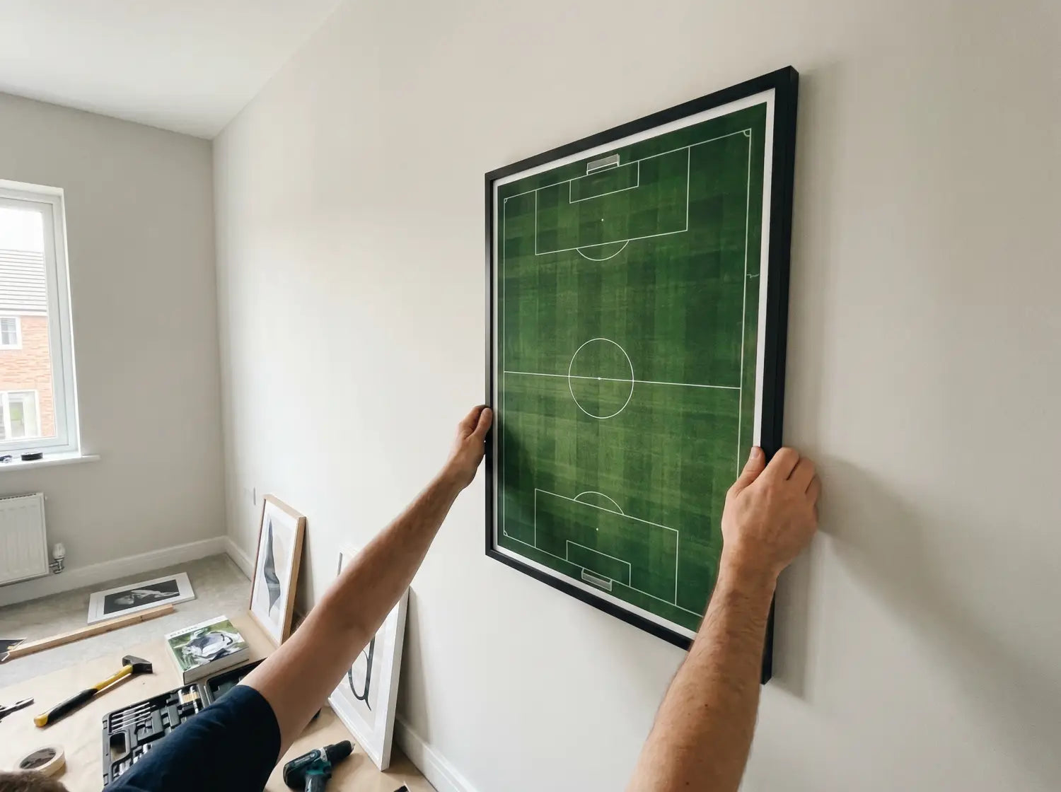 Parent ajustant un poster vue aérienne de terrain de foot sur un mur de chambre