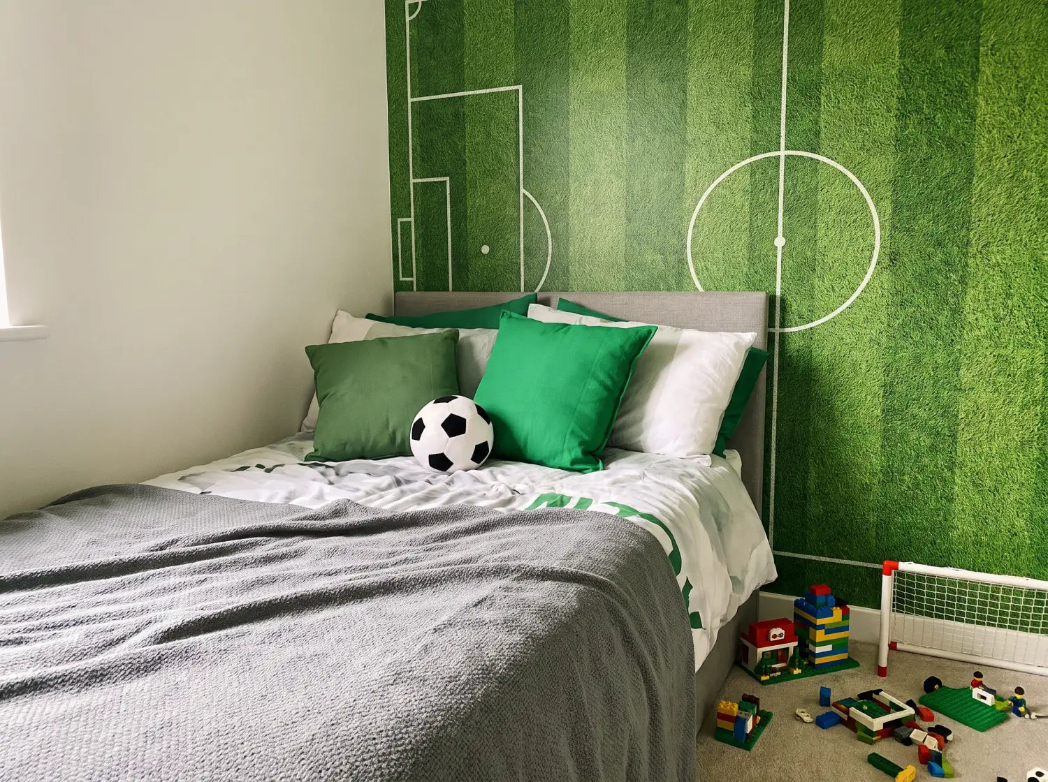 Coin lit d'une chambre enfant avec papier peint terrain de football et coussins verts