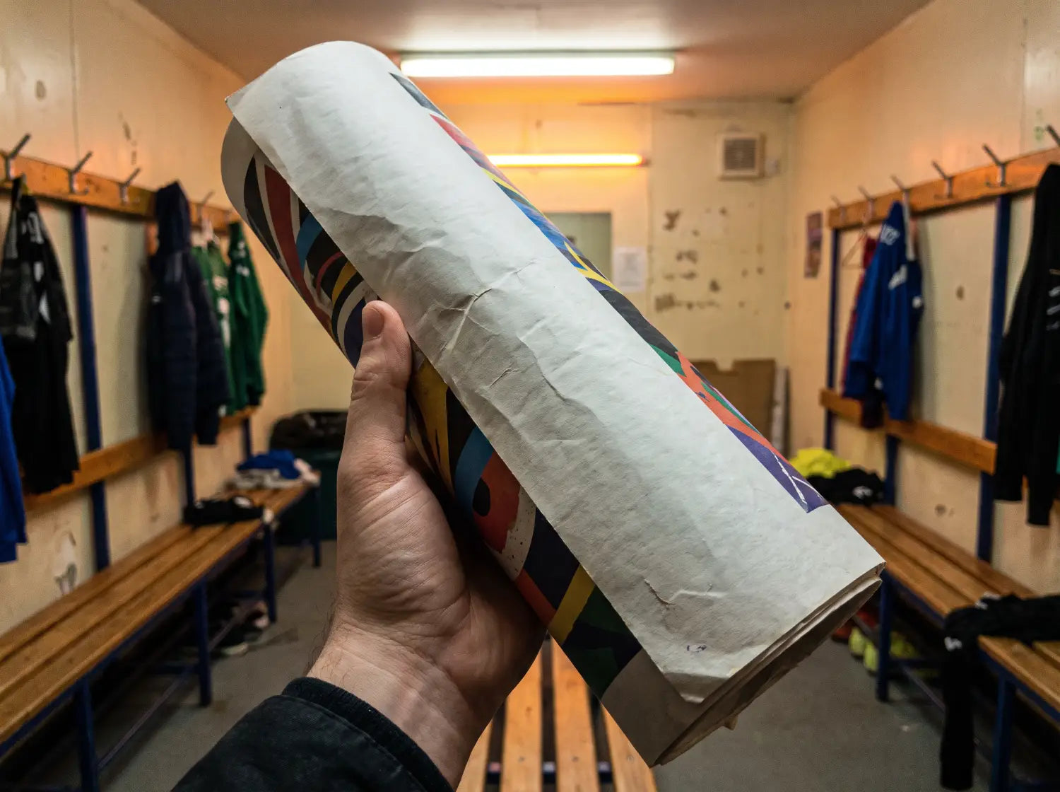 Affiche grand format enroulée tenue à la main dans un vestiaire de club de football amateur
