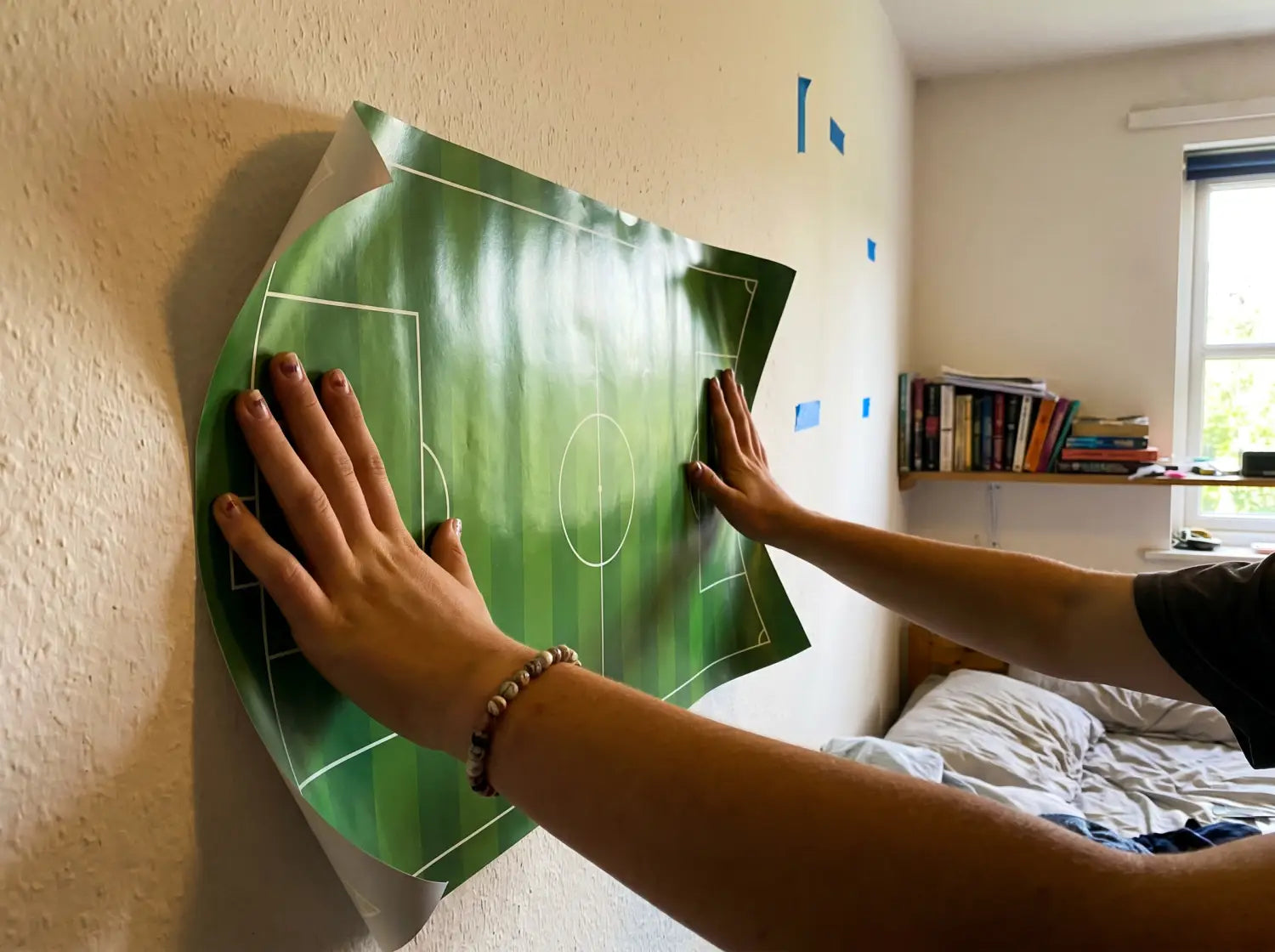 Ado positionnant un grand poster de foot contre le mur de sa chambre