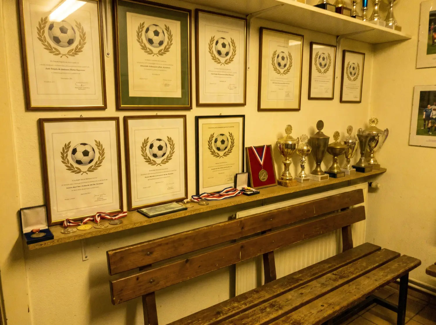 Mur de club house de foot amateur décoré de diplômes encadrés et trophées
